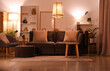 © Pixel-Shot - Interior of modern living room with grey sofa, armchair, pouf and glowing lamps at evening