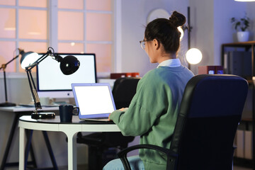 Wall Mural - young woman working with laptop at office in evening, back view