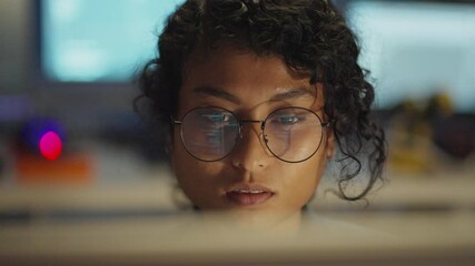 Asian programmer deep in thought, her professional aura illuminated in dim tech light.
