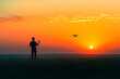 © Winda - Man Piloting a Drone with a Remote, Framed by a Colorful Sunset