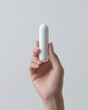 © Roberto - A clean, minimalist close-up of a hand holding a sleek white capsule container, representing medicine, supplements, or personal care products.