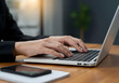© Jus - Close-Up of Woman's Hands Typing on Laptop at Wooden Desk with Smartphone and Notepad