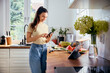 © baranq - Woman in kitchen reading recipe on her phone while preparing healthy meal