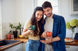 © baranq - Excited couple looking at mobile phone in kitchen while having coffee