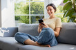 © baranq - Woman with mobile phone sitting on sofa at home