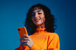 © john - Happy gen z woman using phone in vibrant orange monochromatic setting against blue background