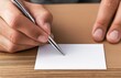 © PirisaTK - A person is writing on a blank card with a pen, resting it on a wooden surface, conveying a moment of creation or communication.