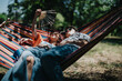 © qunica.com - Couple relaxing on a colorful hammock in the park, enjoying a sunny day, leisure time, and the beauty of nature together.