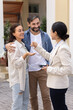 © fizkes - Happy Latin family couple getting new home, taking key from realtor woman, standing outside of new house, receiving accommodation from real estate agent, laughing. Vertical shot