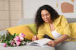 © Pixel-Shot - Young African-American woman with tulips reading magazine at home on spring day