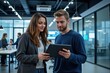 © velikiyzayats - Engaged Young Female and Male Professionals Collaborating over a Tablet in a Modern Office Environment with Peers in the Background
