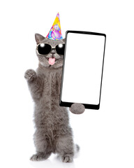 Poster - Happy cat with tongiye out wearing sunglasses and party cap standing on hind legs and shows big smartphone with blank screen. Empty space for text. isolated on white background