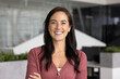 © fizkes - Cheerful beautiful Latin business leader woman looking at camera, keeping arms crosses, posing for front head shot portrait. Happy female successful professional standing in office space alone