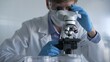 © volha_r - Male scientist researcher wearing blue gloves, protective glasses and medical mask, is using microscope in modern laboratory, portrait view. Low key lighting photo. Science and Medicine