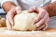 © bcendet - Baker's hands shaping a ball of dough on a wooden surface