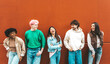 © Davide Angelini - Happy multiracial friends standing over isolated background - Cheerful young people socializing outdoors - University students laughing together on red wall - Youth culture and friendship concept