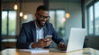 © Jutha - Busy Young African Businessman: A Professional Entrepreneur Using Smartphone and Laptop for Financial Banking Apps in a Modern Office - Vector Illustration