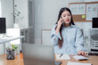 © MINAE - Businesswoman managing her office tasks, using a calculator and talking on the phone while working at her desk. Engaging in finance and communication in a modern, organized workspace