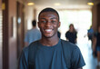 © Easy - An attractive young Black man stands in a well-lit hallway, smiling brightly while wearing a backpack. Students move past him, creating a lively atmosphere as he enjoys his day