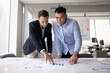© fizkes - Two multiethnic businessmen developing marketing strategy for project, analyzing financial statistic reports, sales benchmarks, reviewing papers with diagrams on large table