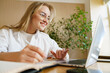 © muse studio - Young woman studying at a desk with laptop and notebook in a bright, cozy room during the day