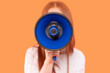 © Iryna - Individual holds a megaphone against a vibrant orange backdrop while promoting a message during a lively gathering in a public space