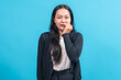 © Saddha Visual - Asian woman with long black hair wearing a black cardigan and white shirt, biting her nails with a worried expression against a blue background, expressing anxiety or nervousness.