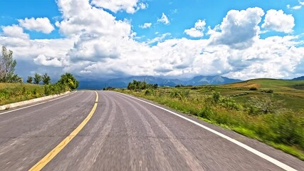 Wall Mural - view from a moving vehicle down an empty rural asphalt road towards distant mountains under a cloudy