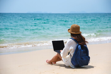 Wall Mural - a female traveler using and working on laptop computer while sitting on the beach