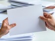 © taweesak - A person holding a blank sheet of paper above a stack of documents, perfect for business or creative concepts