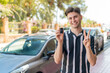 © luismolinero - Young handsome man holding car keys at outdoors smiling and showing victory sign