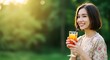 © dreamdes - Young asian woman enjoying refreshing orange cocktail outdoors at sunset. Natural summer portrait with blurred green background and golden light for lifestyle concept.