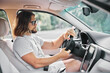 © SHOTPRIME STUDIO - Young man driving a car focused on the road and enjoying the journey Soft background with greenery Stylish interior with modern design elements