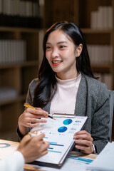 Fototapete - Asian businesswoman pointing at charts and graphs discussing project strategy with colleague in office meeting