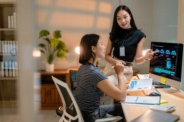 Fototapete - Asian businesswomen discussing marketing strategy pointing at computer screen working late at night in office