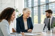 © DND - A senior female executive working on a laptop, strategizing business plans with colleagues.