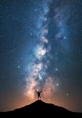 Wall Mural - milky way and happy man with raised up arms on the mountain peak at starry night. silhouette of guy,