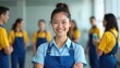 © Vadym - Portrait of cheerful asian cleaning lady in blue uniform and apron. Woman stands with crossed arms smiling at camera with cleaning staff behind. Housekeeping service team provides pro office cleaning.