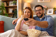 © Graphicroyalty - A happy couple enjoys a cozy movie night at home, sitting on the couch with a bowl of popcorn. They are smiling and engaged, sharing a fun and relaxing evening together.