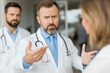 © AlienCat - Concerned male doctor discussing with colleague in hospital setting. Serious-looking doctor in white coat, gesturing during discussion with another medical professional, indicating concern.