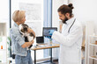 © sofiko14 - Veterinarian explaining X-ray image to young woman holding her pet cat indoors office. Image suitable for health care, veterinarian services, and animal welfare.