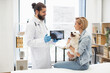 © sofiko14 - Veterinarian showing X-ray results to young adult woman holding small white dog in clinic. Image portrays care, trust, veterinary medicine. Female wearing casual attire, vet in uniform with gloves.
