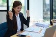 © Jirapong - Confident business woman smiling Show successful gestures at her desk with market charts and documents in office