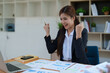© Jirapong - Confident business woman smiling Show successful gestures at her desk with market charts and documents in office