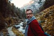 © vernStudio - A man with a backpack, in a red sweater, takes a selfie during a trip, standing against the backdrop of a mountain. The man enjoys the picturesque view. The concept of traveling, active lifestyle