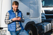 © Serhii - Professional driver using mobile phone while standing in front of his truck. Copy space