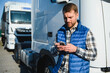 © Serhii - Professional driver using mobile phone while standing in front of his truck. Copy space