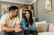 © La Famiglia - Worried couple arguing and discussing problems sitting on sofa at home