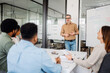 © Vadim Pastuh - A professional business coach leads a strategic planning session in office. A diverse team listens attentively, taking notes and engaging in discussion. Teamwork, leadership, and professional growth.
