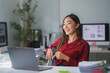 © Crystal - Young happy Asian businesswoman smiling and working with laptop computer in modern office, looking away from the screen
